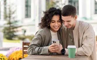 A smiling couple looking at a phone together at a cafe table