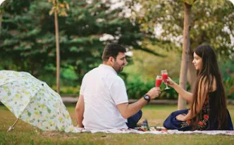 Two people toasting on a picnic blanket in a park